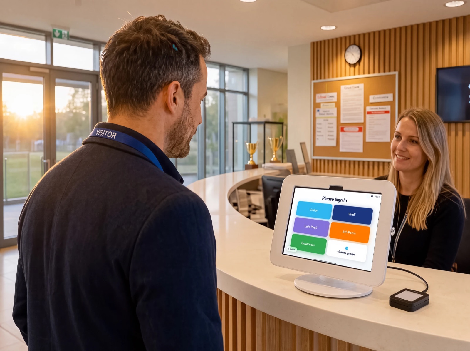 A visitor signing in on the OnSite iPad at a school reception desk while the receptionist looks on